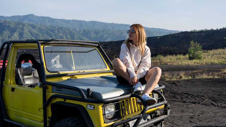 A woman sits on a Jeep on a national park road