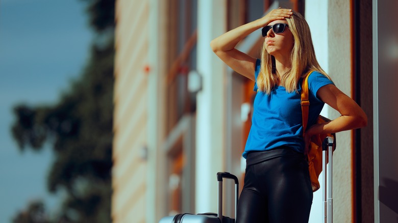 Worried female traveler waiting with her luggage outside
