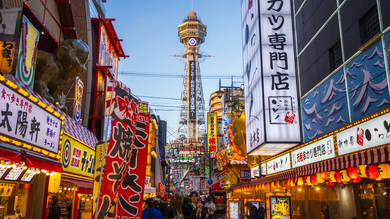 Vibrant street with bright lit neon signs in Japanese on both sides and a satellite tower ahead