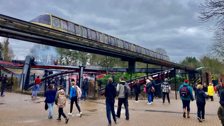 Yellow monorail train running above ground while people walk in theme park