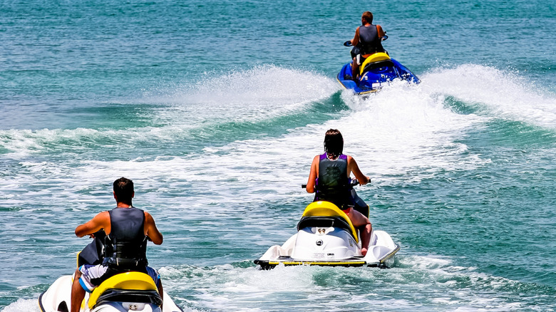 People riding solo on jet skis slowly through the water with life vests in the Bahamas.