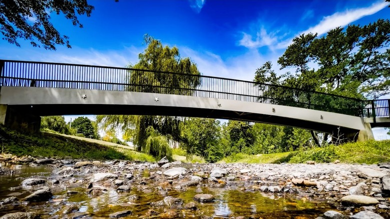 A bridge spanning over a creek with a rocky bed at a park in Trumbull, Connecticut, surrounded by greenery.
