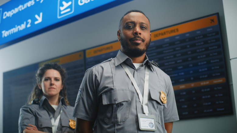 Two TSA officers standing and looking into the camera with unhappy expressions on their faces.