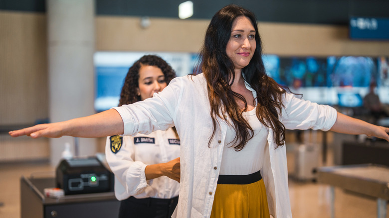 A young Hispanic female airport security worker scans a smiling female passenger with a wand at a checkpoint