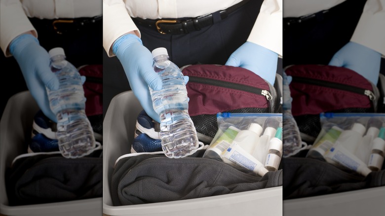 Security holding a bottle of water from someone's luggage.