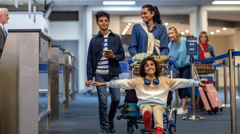 A smiling family pushing their bag trolley at the airport.