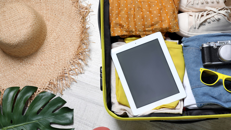 A suitcase packed for vacation with a tablet on top of the clothes