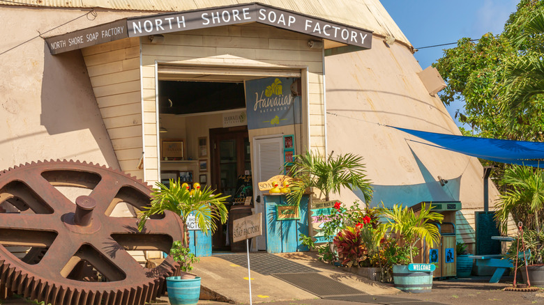 Front entrance of the North Shore Soap Factory at the Old Waialua Sugar Mill, with a giant metal gear in the front, and other bright signage.