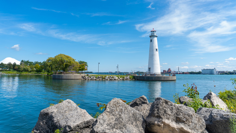 The Milliken State Park Lighthouse rises over grass, rocks, and an inlet on a clear summer day in Detroit