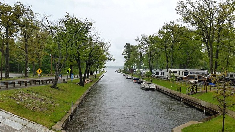 A long shot of the canal that connects lakes Cadillac and Mitchell, with trees and grass on both sides and boats and campers on the left side.