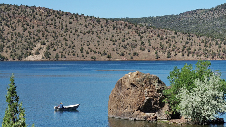 Boat out on Prineville Reservoir in front of stretches of hilly terrain.