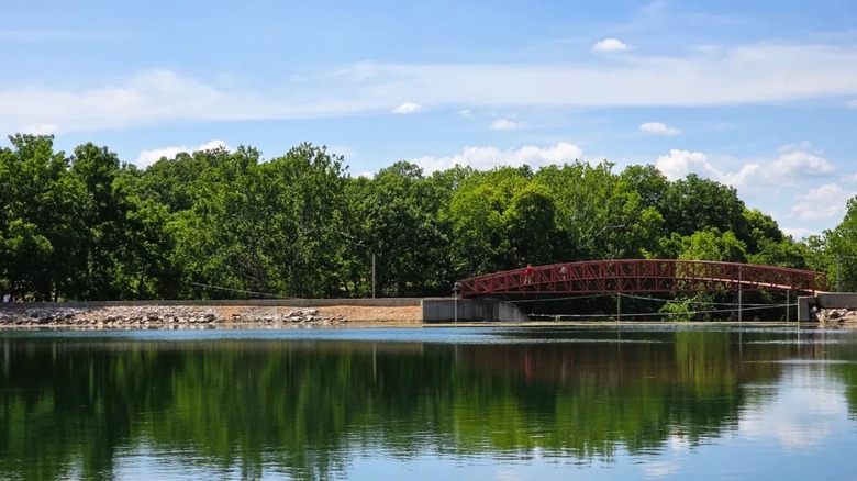 A pedestrian bridge spans across Valley Water Mill Pond in Springfield Missouri, with reflections of the trees on the glassy water.