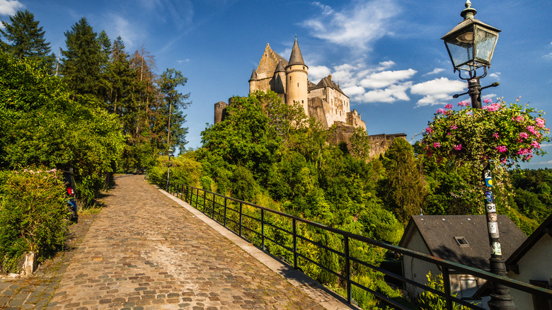 Uphill path through green trees flanking the medieval Vianden Castle in Luxembourg.