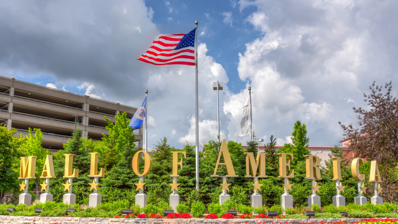 An American flag flies over the golden Mall of America sign at the entrance.