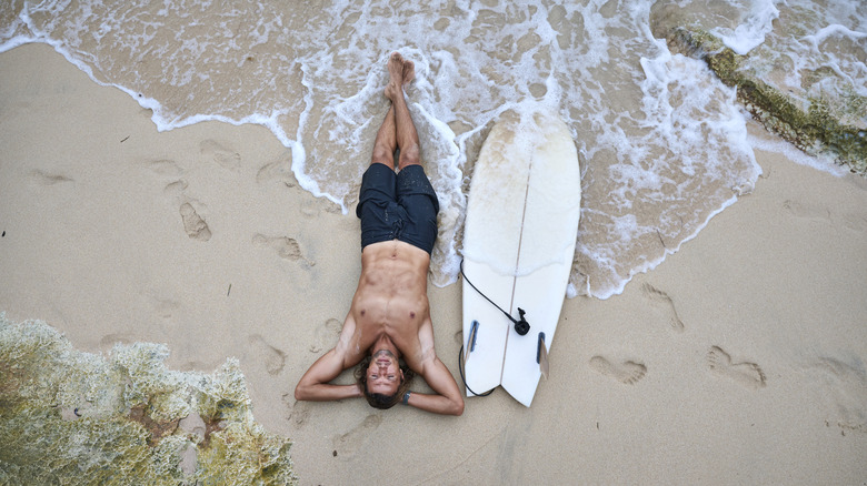 Surfer lying on sand next to a surfboard