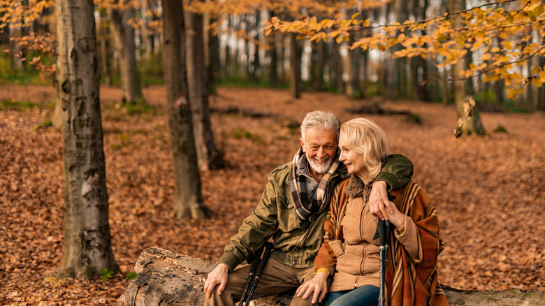 Retired couple sitting on log in autumn woods