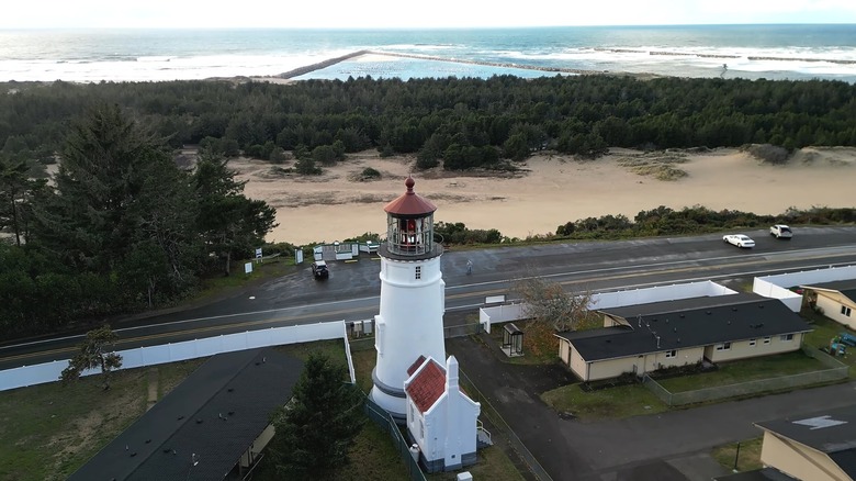 A white lighthouse sits along the road with the ocean behind it