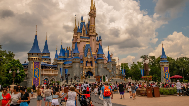 Exterior view of the castle at Magic Kingdom Park in Walt Disney World in Orlando, Florida, USA and a crowd of people outside it on a bright sunny day.
