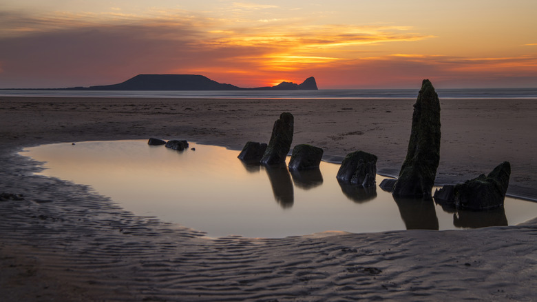 Shipwreck remains with Worm's Head in distance at Rhossili Bay Beach, Wales during sunset