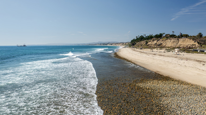 View across Trestles Beach capturing the waves, pebbles, sand, bluffs, and trees on a sunny day.