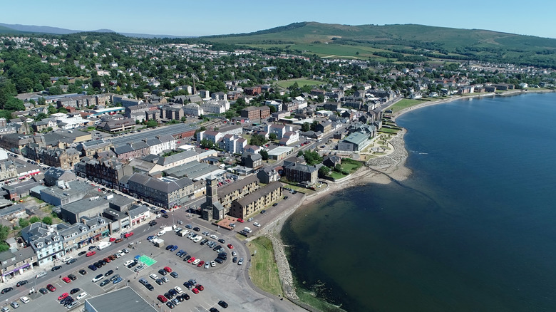 An aerial photo of downtown Helensburgh, with the waterfront, building-lined street running parallel, and the rolling countryside behind