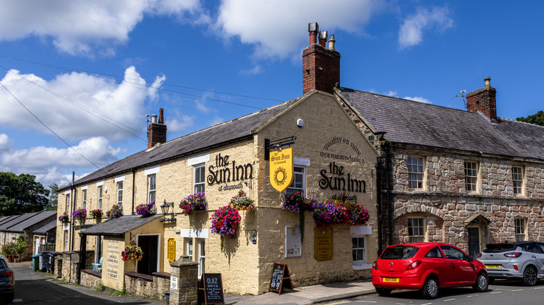 A traditional pub, The Sun Inn, with exposed limestone brick on a sunny day in Alnmouth, England