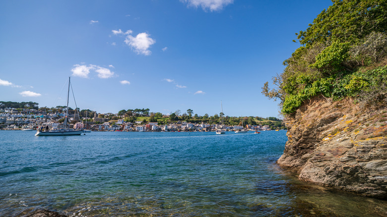 Several boats in the vibrant blue harbor in front of the hills filled with buildings in Fowey, England