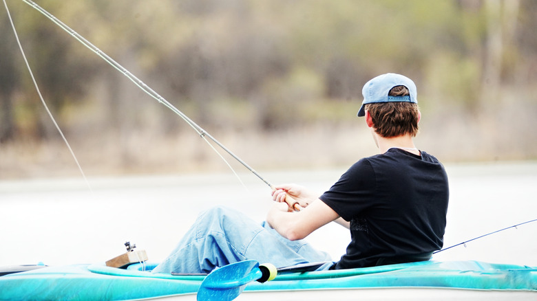 A young man casts a line with his fishing pole while perched in a kayak