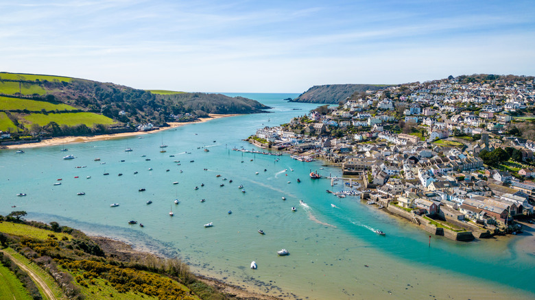 Aerial view of Salcombe with the white buildings of town on the hilly riverside, light blue water, and many boats