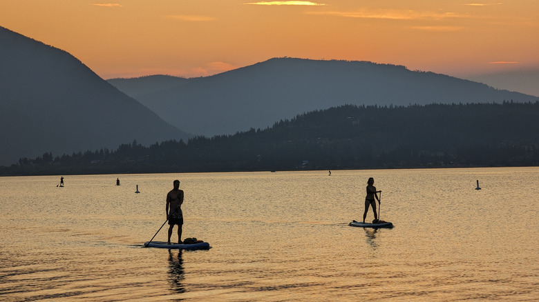 Two people paddle on stand-up paddleboards around a lake at sunset