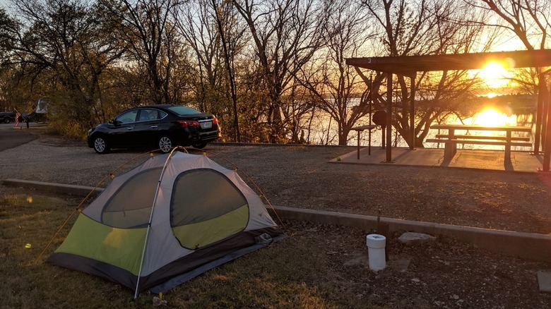 A pitched tent near a picnic area with a parked vehicle in the background during sunset at the Santa Fe Trail campground, Council Grove Lake, Kansas