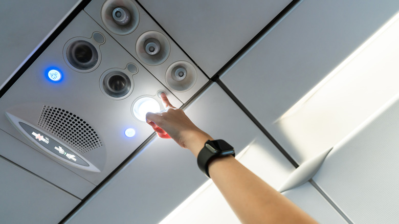 A person fiddling with plane air controls over the seat