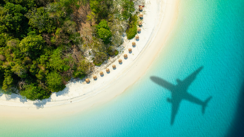 Aerial view of passenger plane silhouette and sandy beach blue sea with waves at sunset.