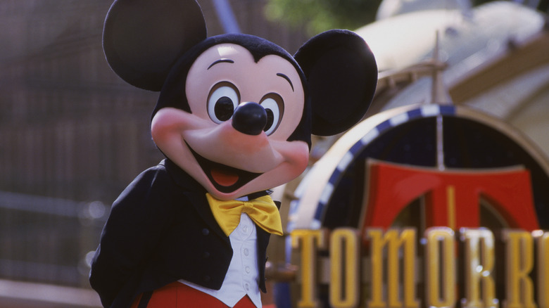 Mickey Mouse standing in front of a Tomorrowland sign