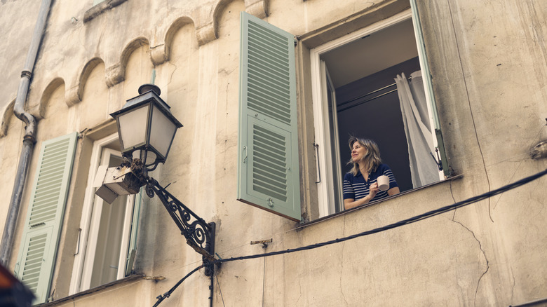 Person looking out of a window in France with a coffee mug in her hands