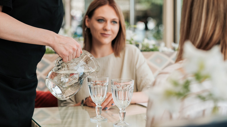 Two women having water poured for them in restaurant