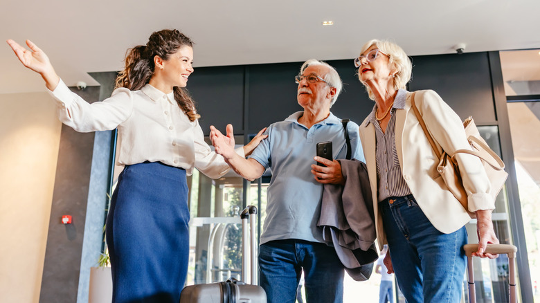 An elderly couple smiles and shakes hands with a hotel staff member in a lobby