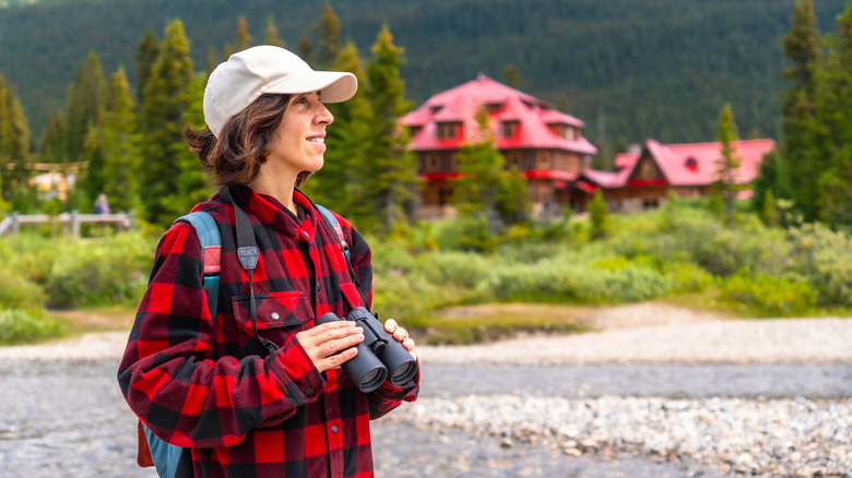 Female tourist holding binoculars, admiring the scenic Num-Ti-Jah Lodge in Banff National Park