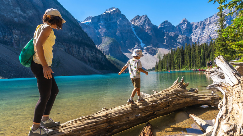 Mother and son balancing on a weathered log over turquoise waters of Moraine Lake