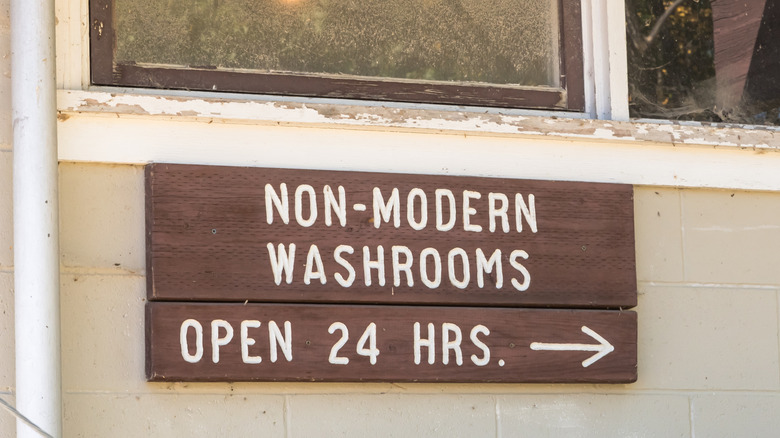 A wooden sign on a building at Winnipeg Beach, Manitoba, Canada, that reads "non-modern washrooms open 24 hours"