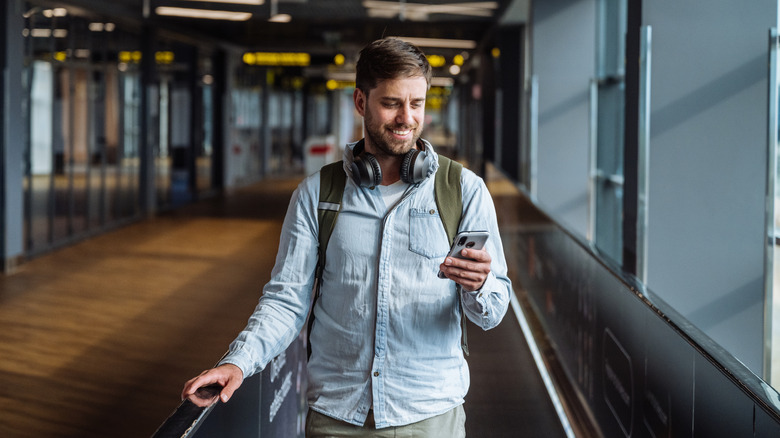 Man walks through airport while looking at phone