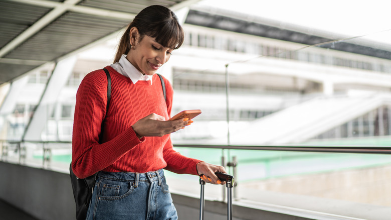 Happy woman uses smartphone while standing in airport