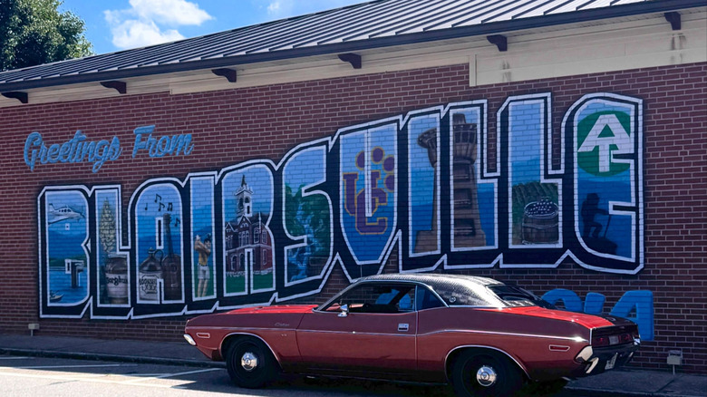 A red car parked in front of a brick wall painted to say greetings from Blairsville, Georgia