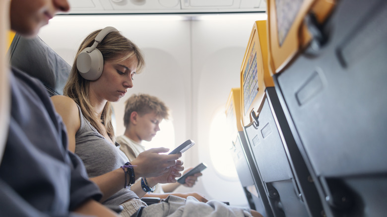People looking at their phones, seated on an airplane