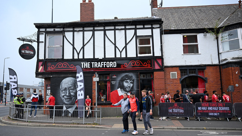 The Trafford pub in Manchester with murals of footballers on the exterior wall. Fans are around the building and loitering in the road.