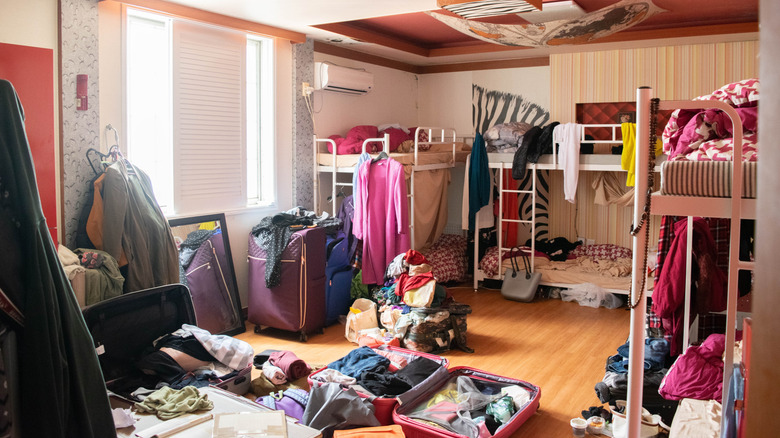 Messy dorm room with bunk beds filled with clothing and luggage