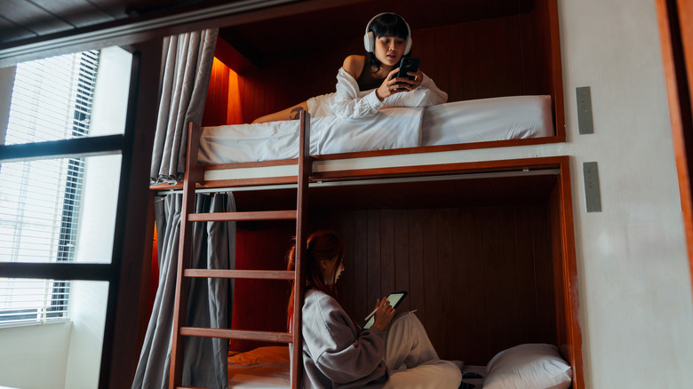 People in dorm beds in hostel wearing headhones and on tablet