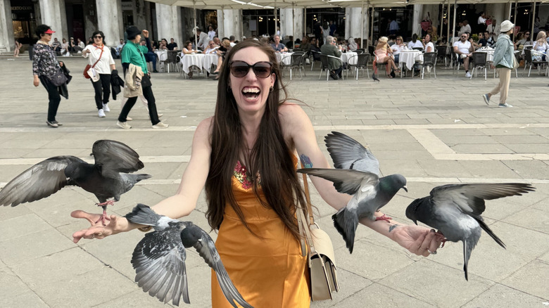 A flock of pigeons converging on a laughing brunette woman in St. Mark's Square, Venice
