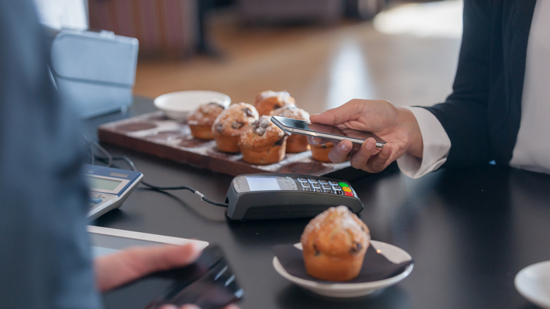 Close up of someone paying for a muffin in a café with his phone.
