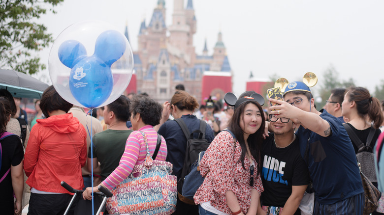 A group of young chinese people taking a selfie with the Enchanted Castle at Shanghai Disneyland